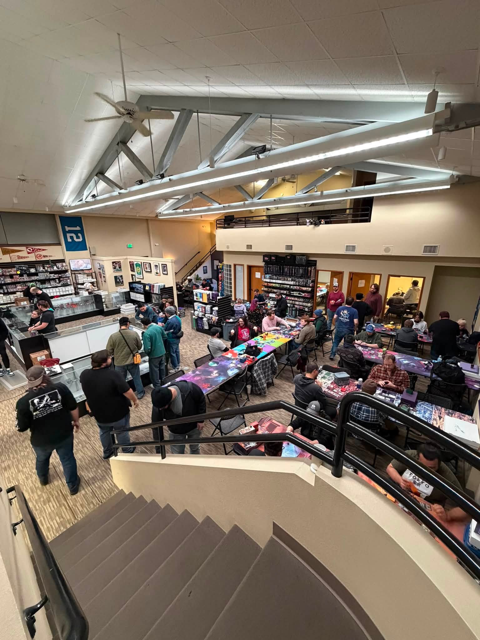 A busy Magic event viewed from the stairs, with players gathered around rows of tables